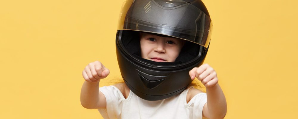 Transportation, extreme, motorsports and activity concept. Portrait of dangerous little girl rider in black protective motorcycle helmet keeping hands in front of her as if driving motorbike